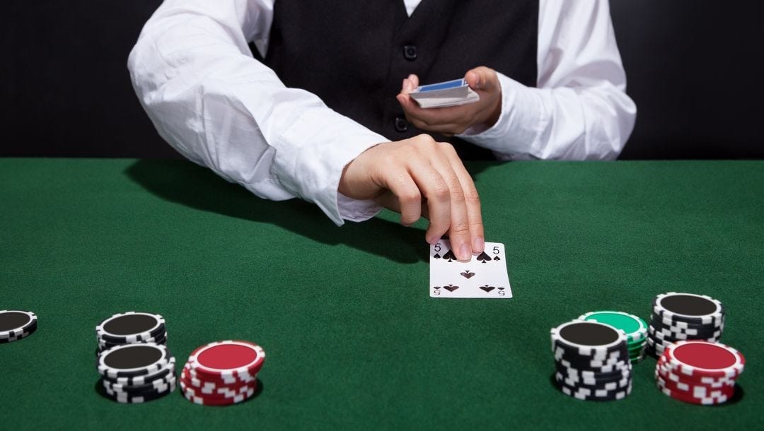 a dealer turns over a five of ace playing card on a green felt poker table with poker chips stacked on it