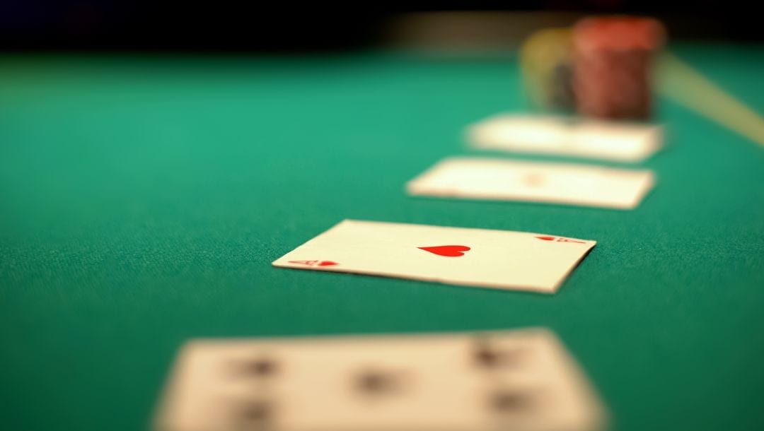 an ace of hearts playing card face up on a green felt poker table with other cards and poker chips blurred around it