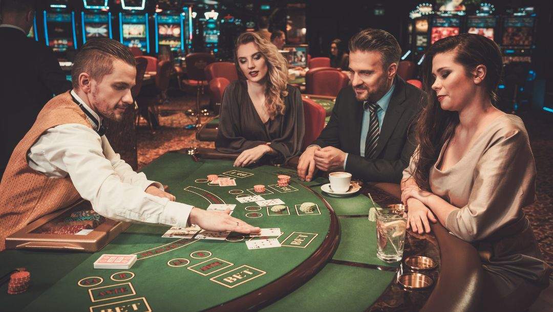 Three players and a croupier at a green felt casino poker table, engaged in a game of poker.