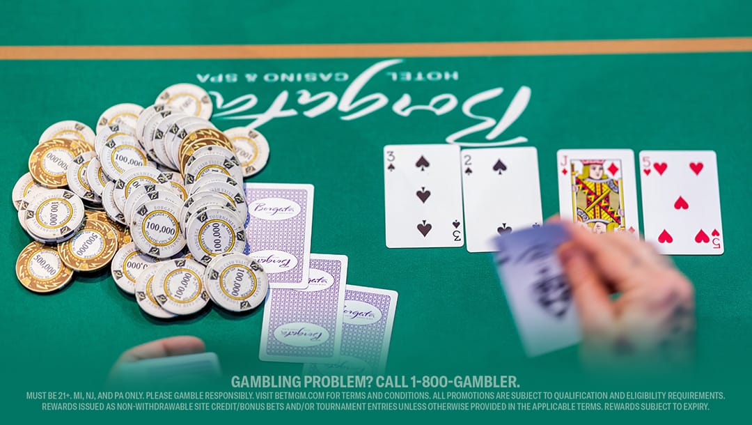 A poker table with a green felt surface, stacked with numerous gold and white chips. Nearby, three playing cards are visible: 4 of spades, 2 of spades, and King of hearts. A blurred hand holds more cards in the foreground.