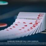 A deck of cards fanned out on a poker table, highlighting hearts. A poker chip and dealer button are blurred in the background.