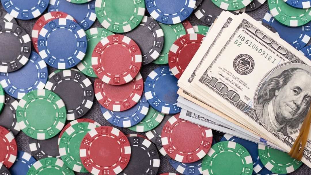 Colorful casino chips spread out on a table, with a stack of $100 bills on top.