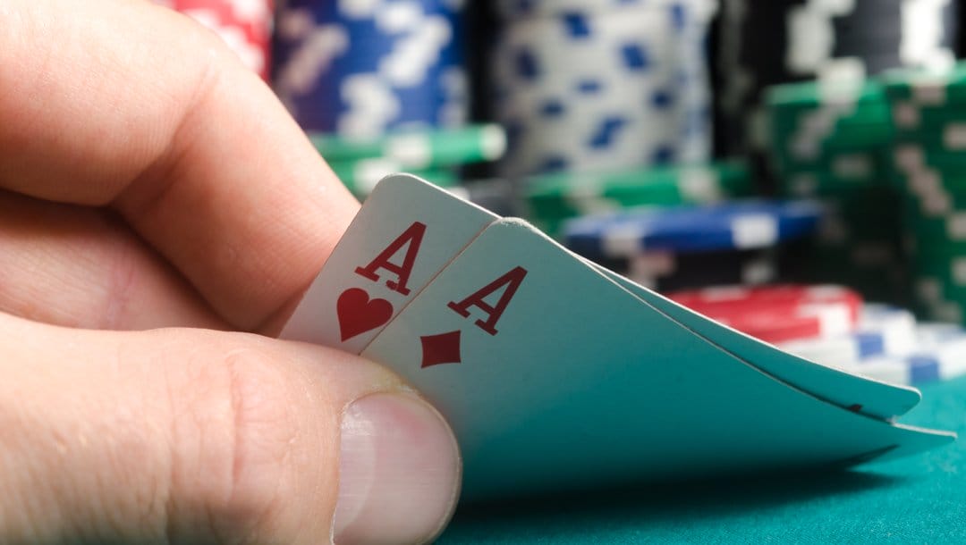A poker player peeks at their hole cards. They have a pair of aces.