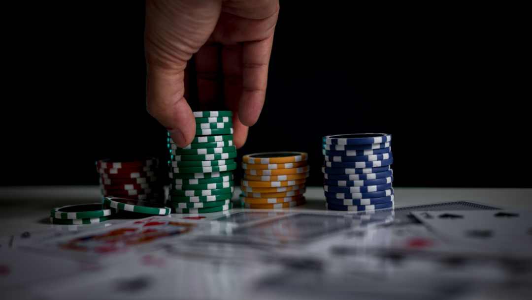 A person picks up some green chips from a poker table with yellow, blue and red chips on the table next to playing cards.