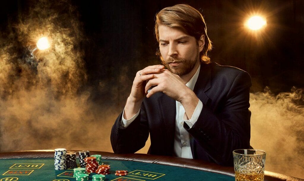 A person sits at a poker table holding their cards while looking at the table pensively.