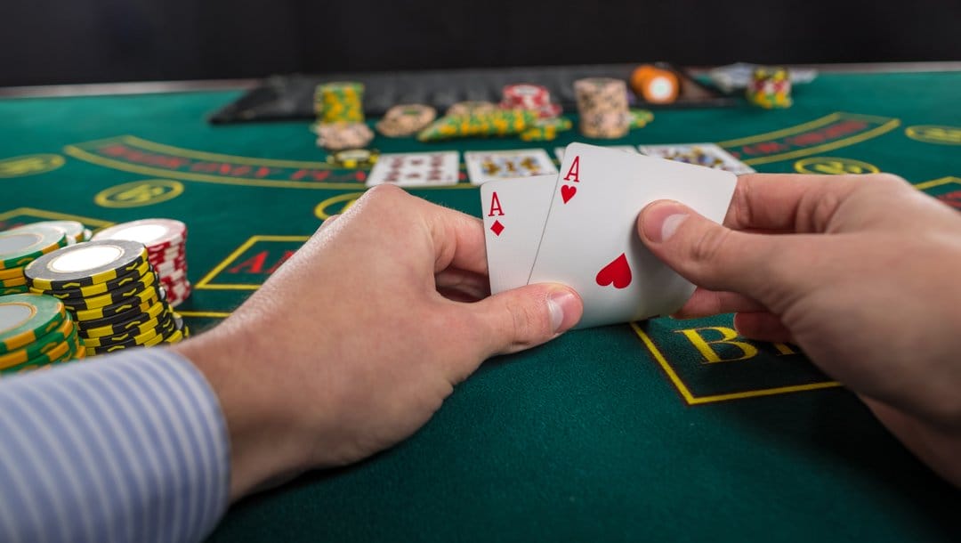 A poker player lifts up their hole cards to look at them. They have a pair of aces.