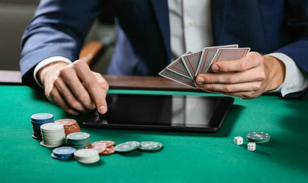 A person using a tablet on a poker table with a hand of cards, and surrounded by poker chips and a pair of dice.