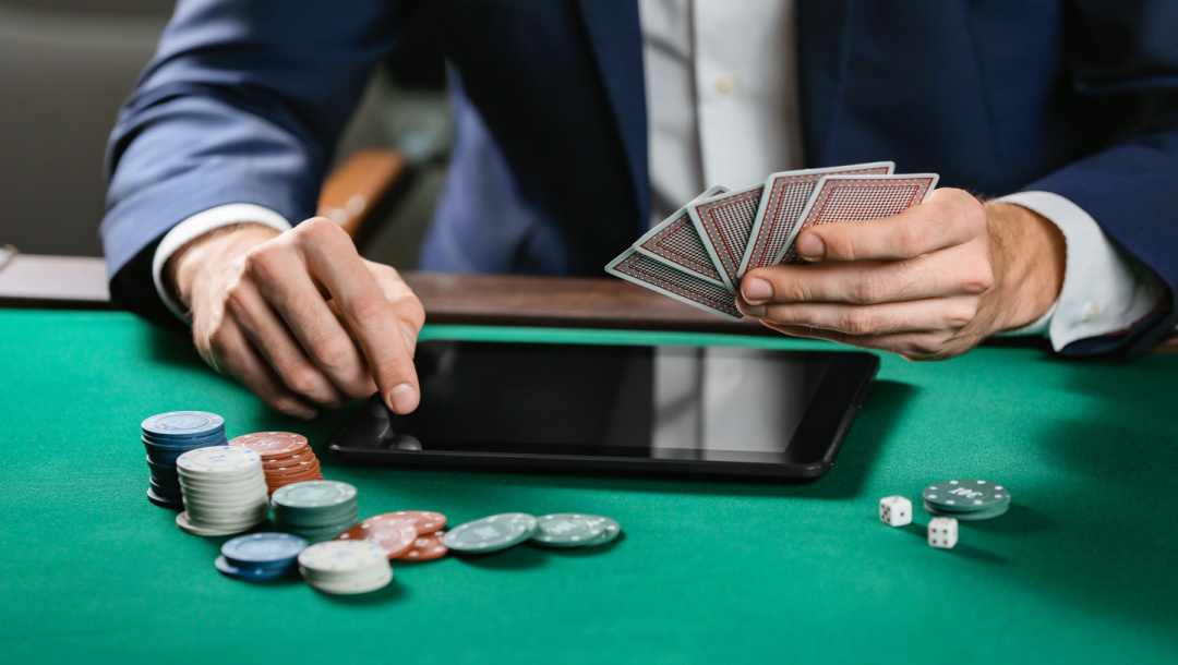A person using a tablet on a poker table with a hand of cards, and surrounded by poker chips and a pair of dice.