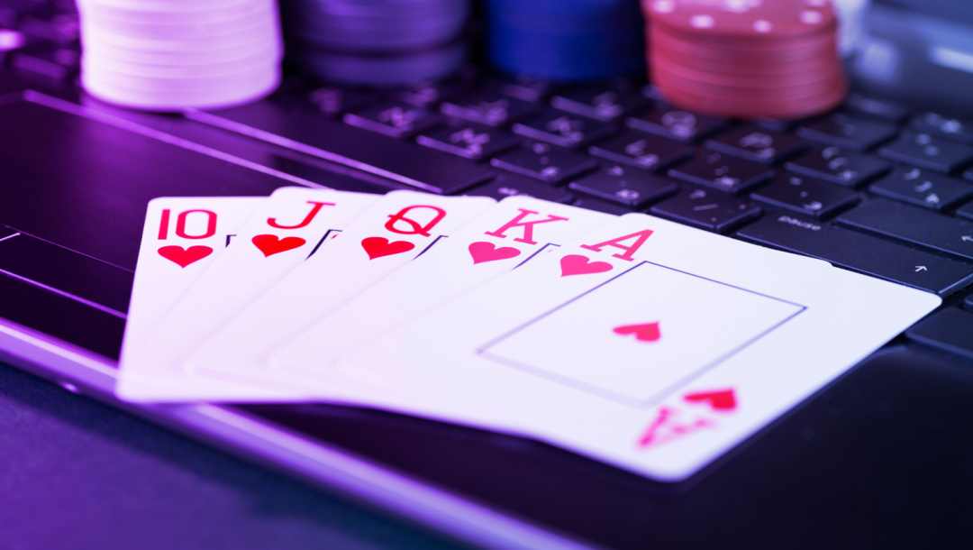 A royal flush of hearts on a keyboard with casino chips in the background and purple hue over it all.
