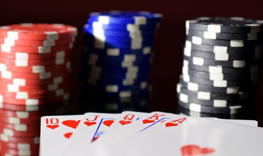 Poker hand royal flush on black reflective board with poker chips on background.