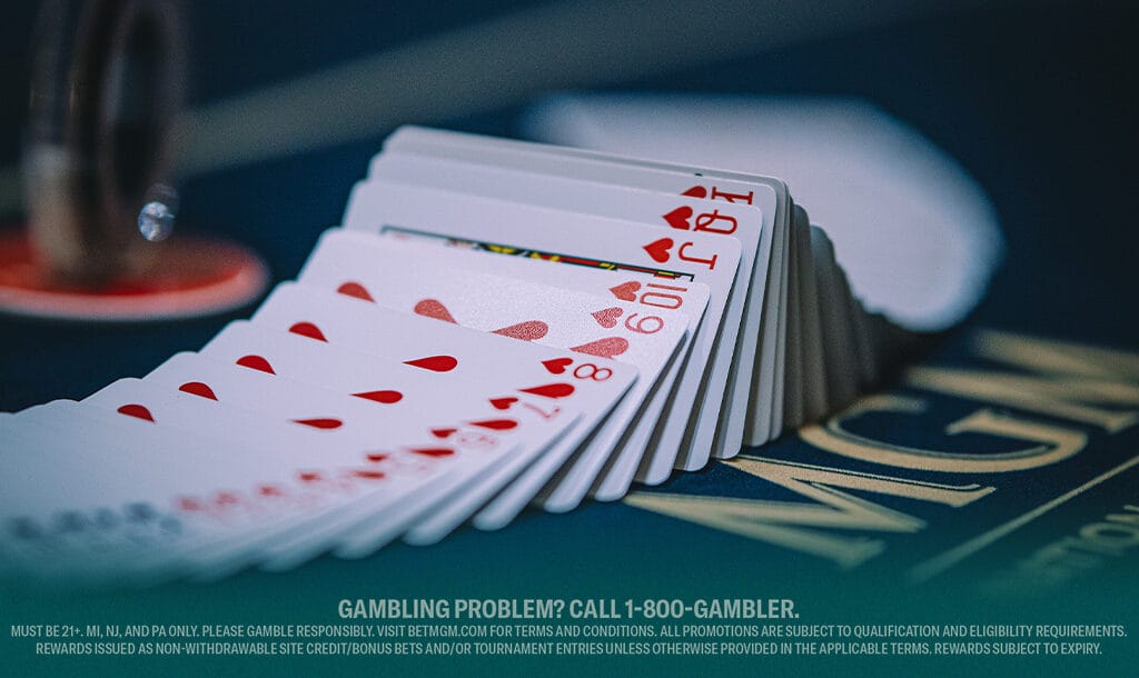 A fanned deck of playing cards, featuring hearts, spreads across a dark poker table. The focus is on a Jack of Hearts.