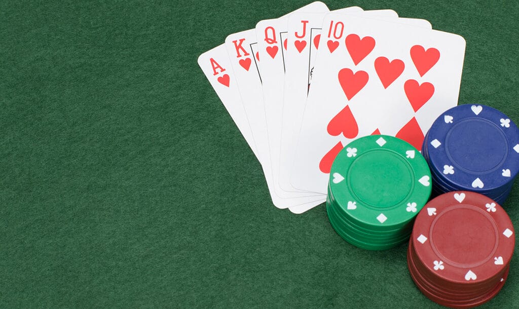 A royal flush in hearts with poker chips on a green felt surface.