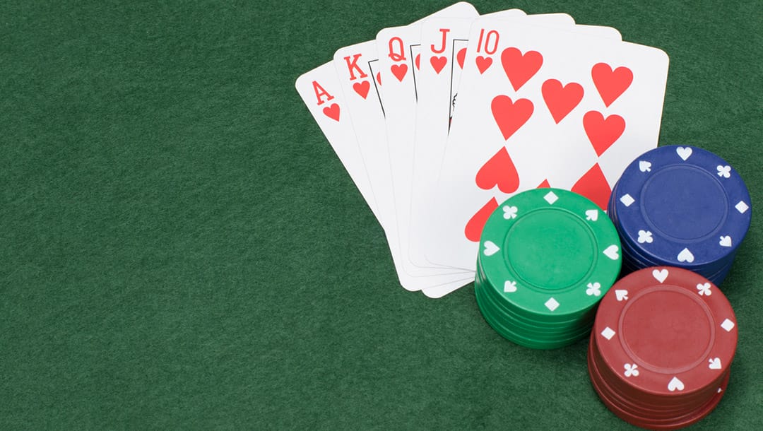 A royal flush in hearts with poker chips on a green felt surface.