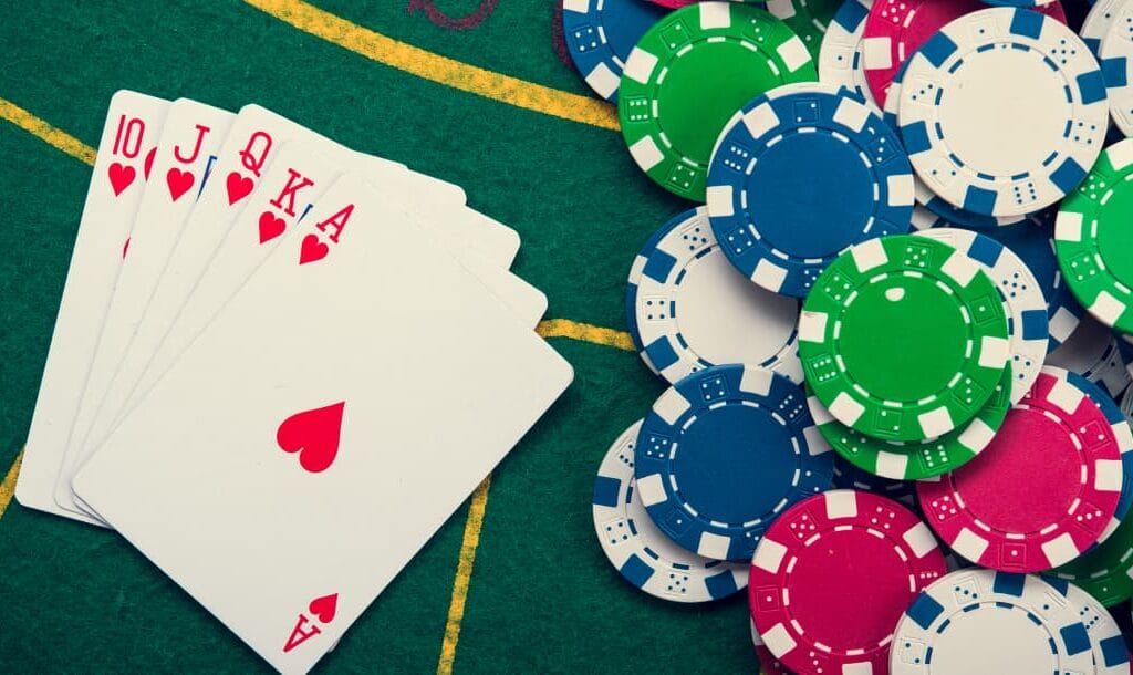 A full suit of Hearts playing cards,and red, white, blue, and green casino chips arranged on a poker table.