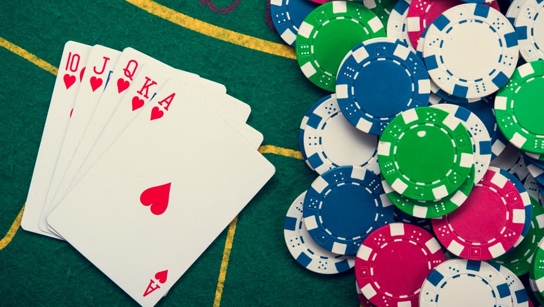 A full suit of Hearts playing cards,and red, white, blue, and green casino chips arranged on a poker table.