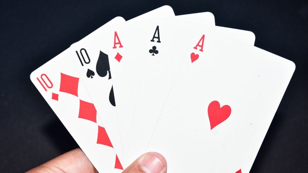 A person holding a Ten of Diamonds, a Ten of Spades, an Ace of Diamonds, an Ace of Clubs, and an Ace of Hearts.