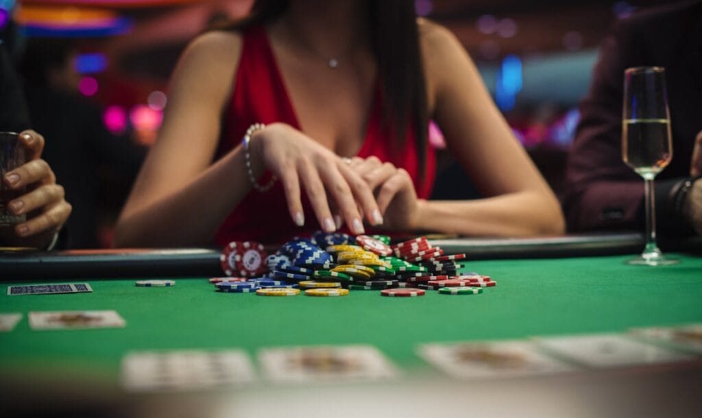 A woman wearing a red dress hovering her hand over colorful casino chips on a green felt poker table.