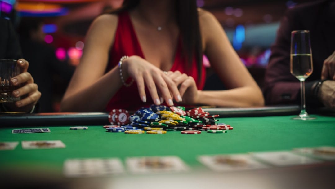 A woman wearing a red dress hovering her hand over colorful casino chips on a green felt poker table.