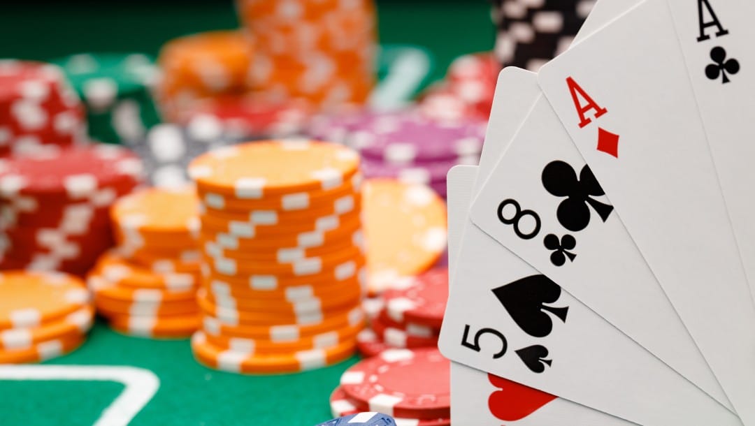 Orange, pink, green and red poker chips with playing cards on a green felt poker table.