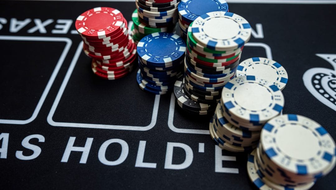 A black Texas Hold’em poker table with red, blue and white casino chips on it.