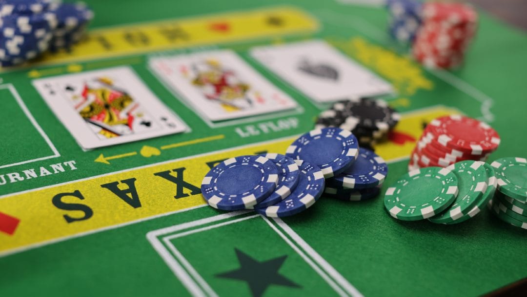 A green Texas Hold’em poker table with casino chips and playing cards on it.