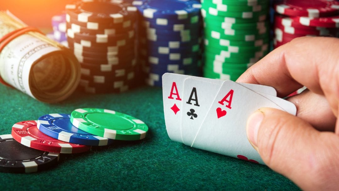 Casino chips and a roll of money on a poker table with a hand holding ace playing cards.