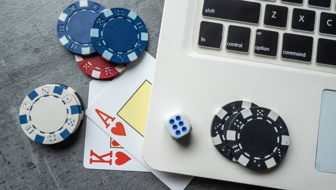 A King of Hearts playing card, an Ace of Hearts playing card, poker chips, a laptop, and a dice arranged on a table.