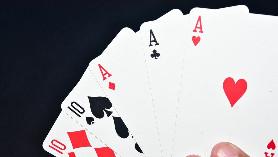 A person holding a ten of diamonds, a ten of spades, an ace of diamonds, an ace of spades, and an ace of hearts.