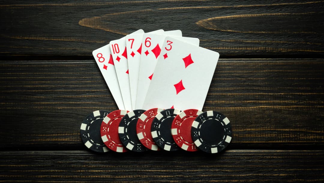 Playing cards with black and red casino chips on a wooden surface.
