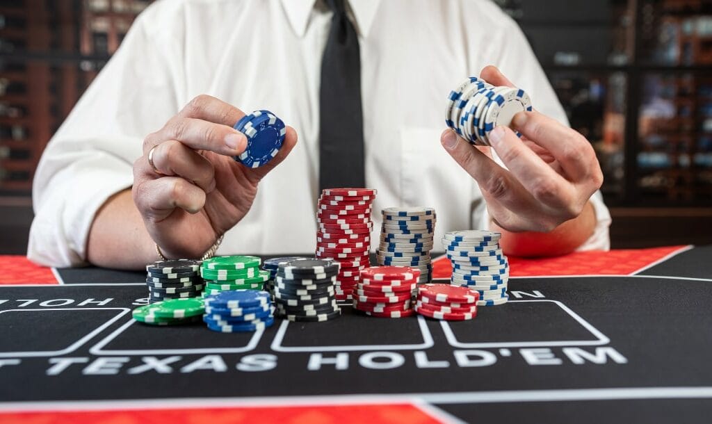 A man wearing a white shirt and black tie holding casino chips on a black and red poker table.