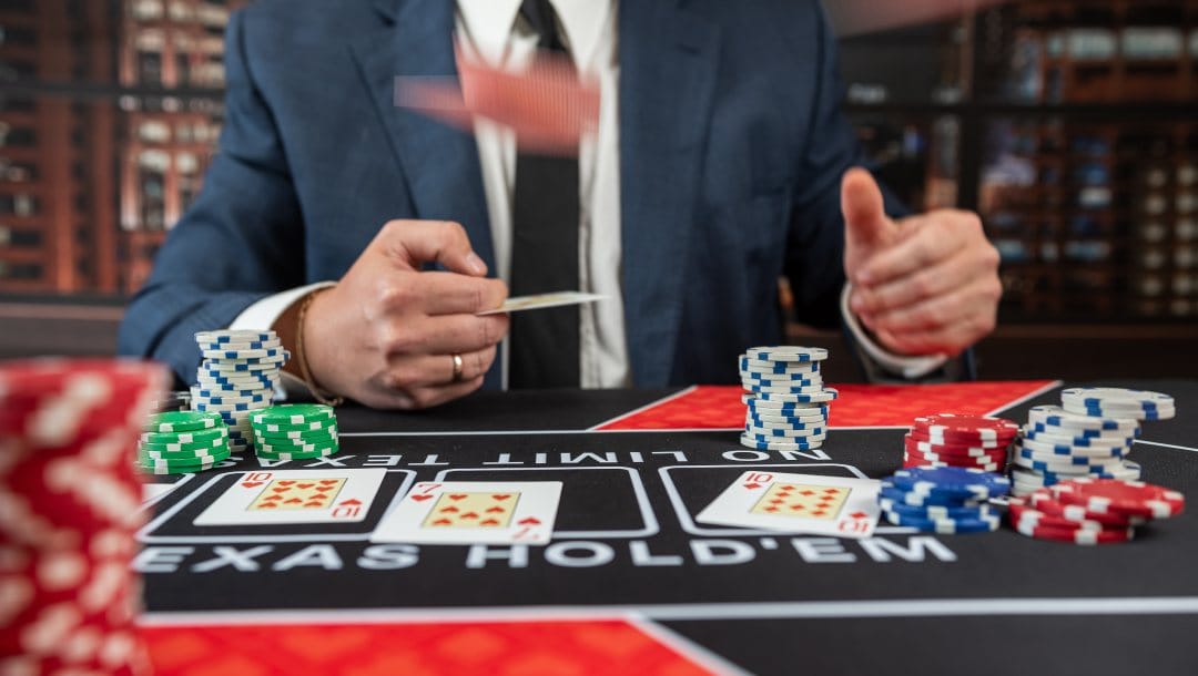 A man wearing a suit and tie throws a playing card on a black and white Texas Hold’em poker table.