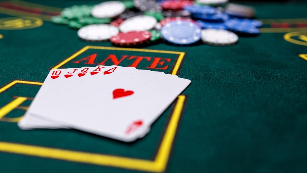 Playing cards and red, green, white, and blue casino chips on a poker table with the word ANTE.