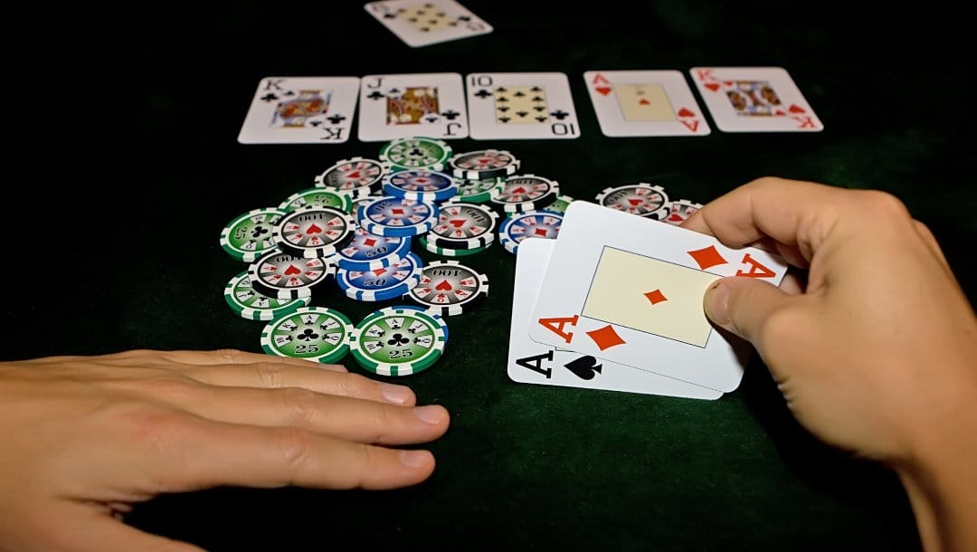 Hands on a black felt table with poker chips and playing cards.