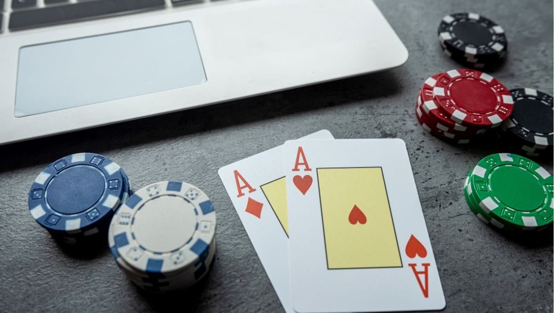 An ace of hearts, and an ace of diamonds, poker chips, and a laptop placed on a table.