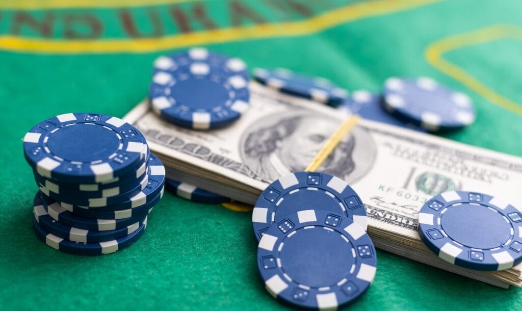Blue poker chips, and a stack of money arranged on a green poker table.