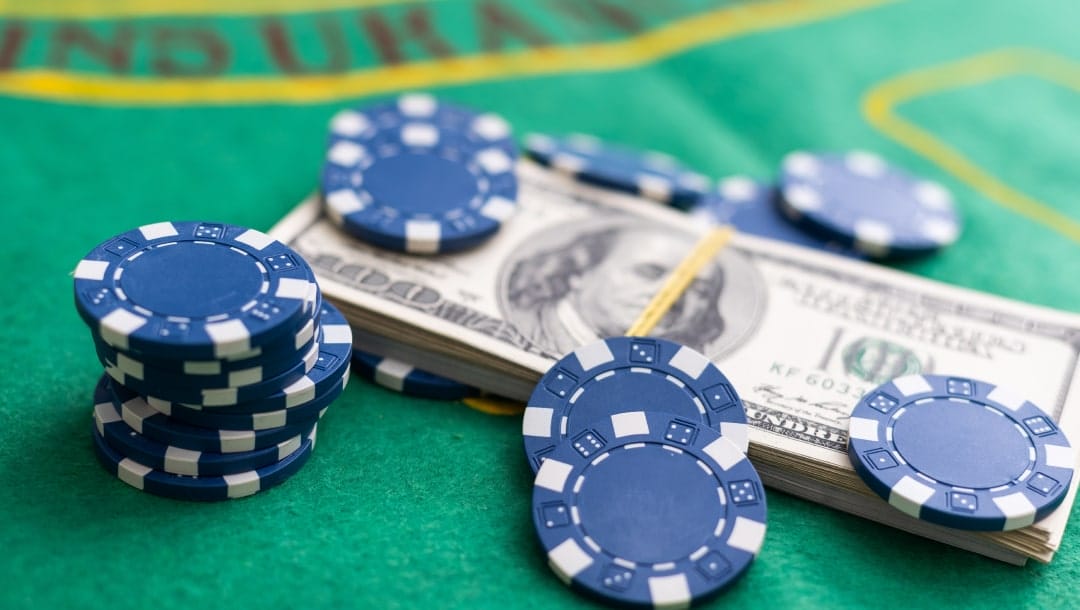 Blue poker chips, and a stack of money arranged on a green poker table.