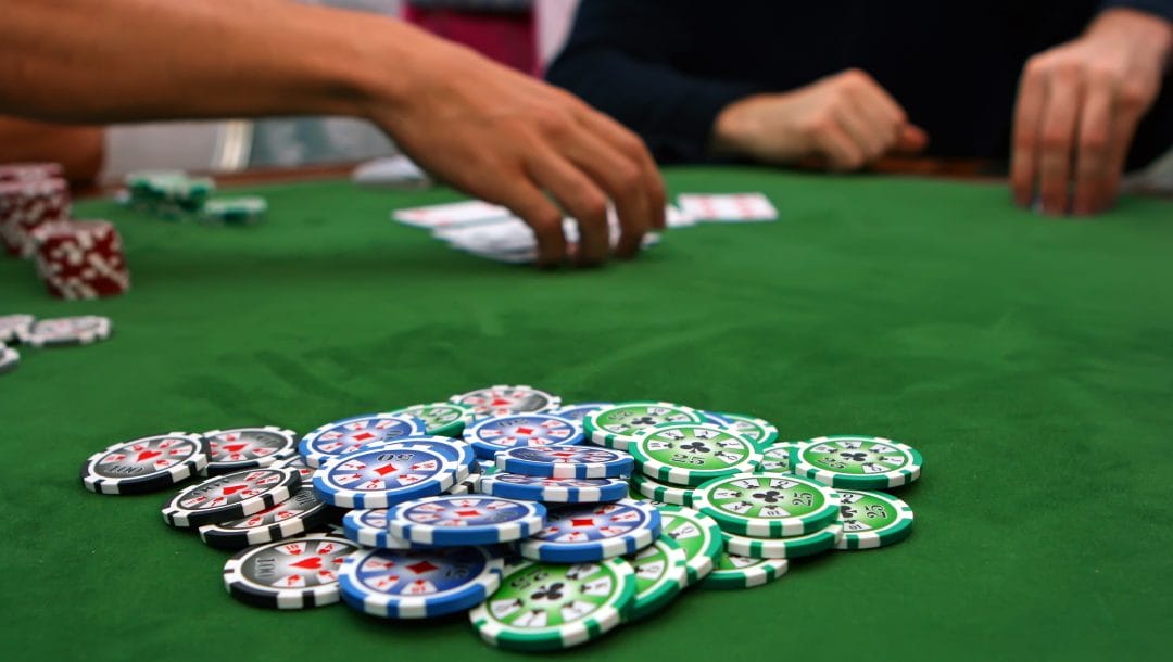 Hands on a table with casino chips and playing cards in view.