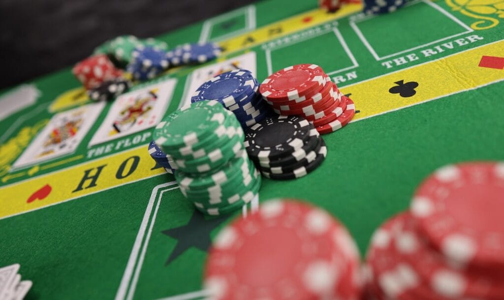 A closeup, slightly angled photograph of of poker chips on a green Texas Hold’Em table.
