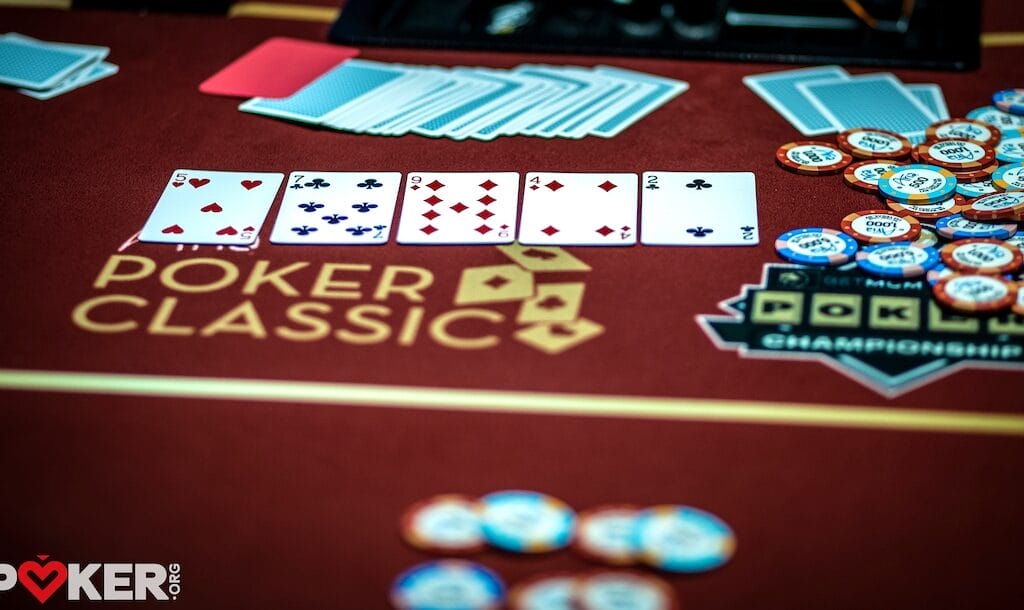 Five playing cards are spread on a poker table with betting chips, indicating an active card game.