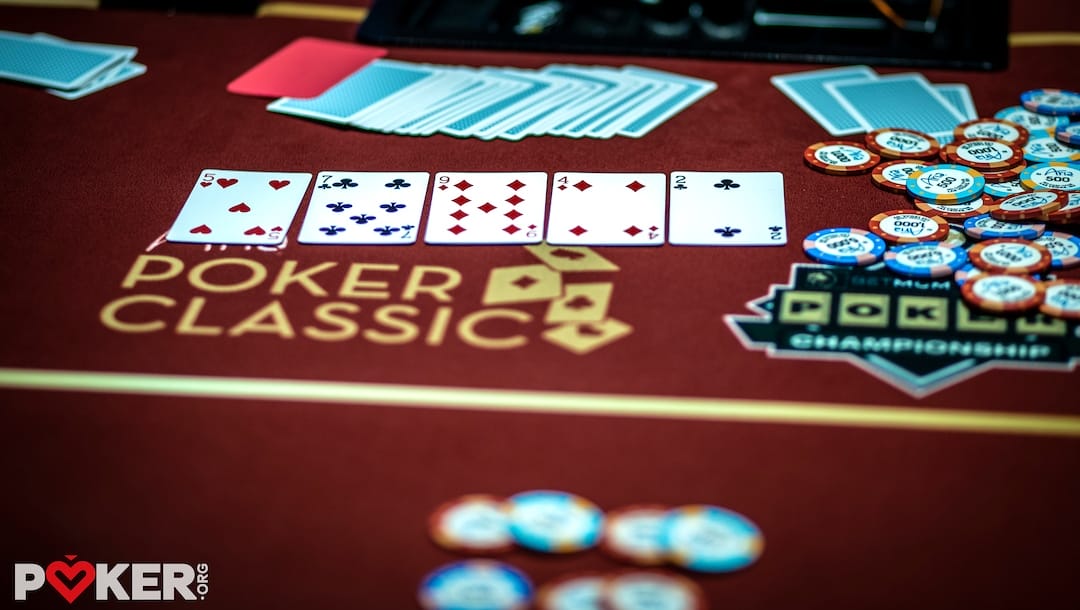 Five playing cards are spread on a poker table with betting chips, indicating an active card game.