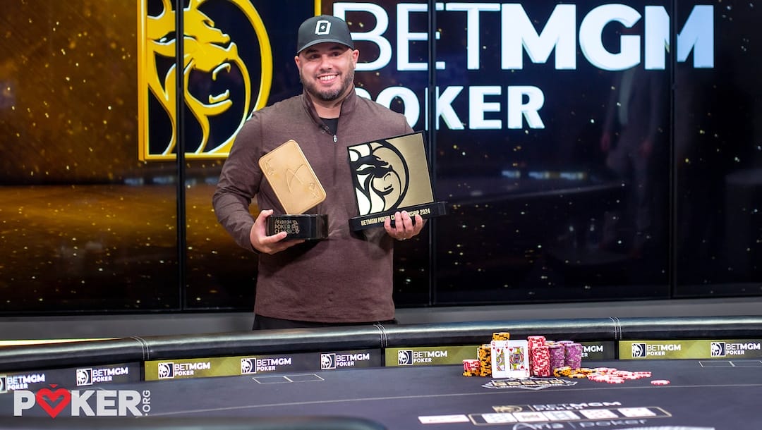 Daniel Maor smiles as he holds awards at a poker table, with chips stacked and a "BetMGM POKER" logo backdrop.