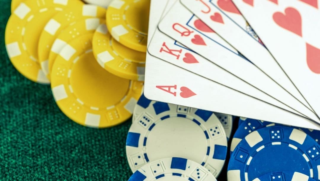 An Ace of Hearts, King of Hearts, Queen of Hearts, Jack of Hearts, and 10 of Hearts arranged in a royal flush, on top of yellow, white, and blue poker chips.