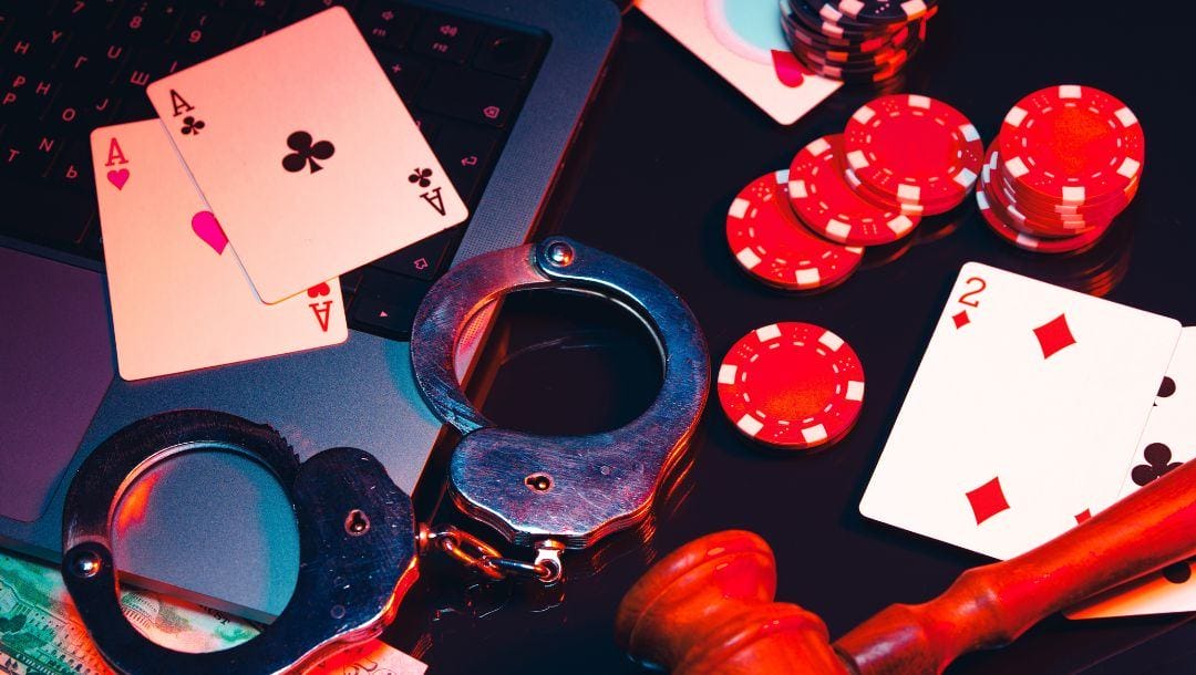 A legal online poker concept image featuring handcuffs, poker chips, playing cards, and a judge’s gavel on and around a laptop.