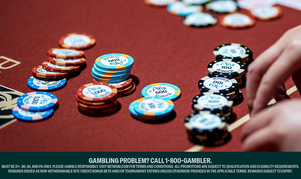 A hand reaches toward stacks of colorful poker chips on a red casino table.