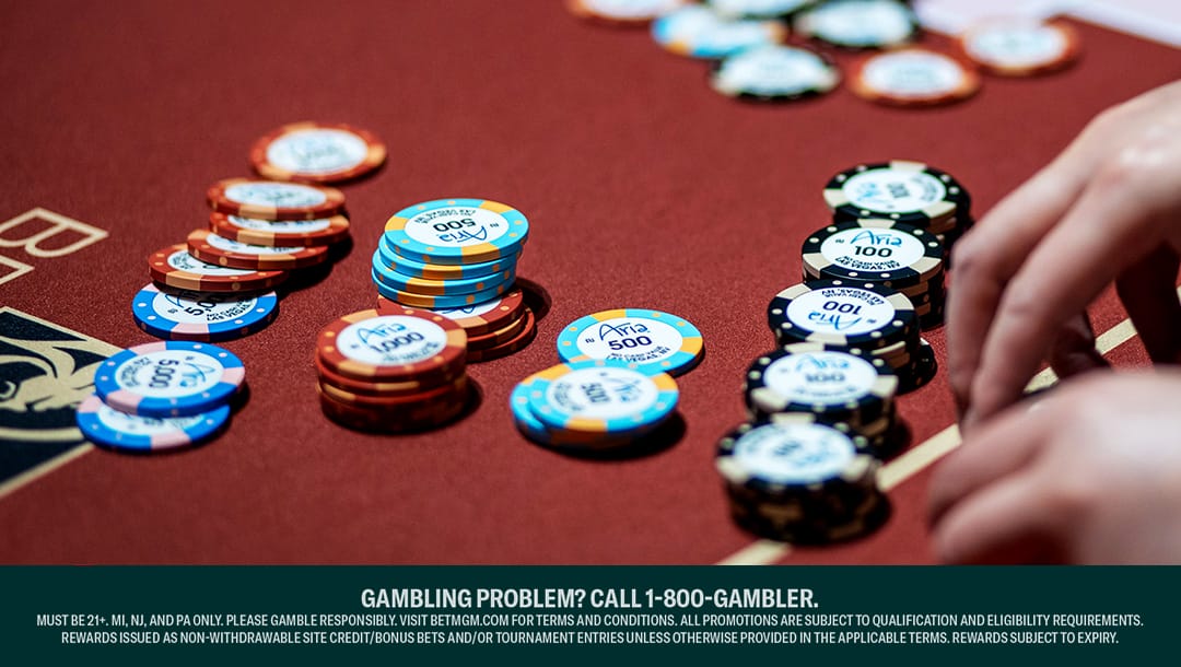 A hand reaches toward stacks of colorful poker chips on a red casino table.