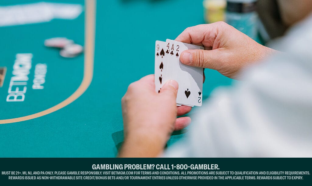 A person holds a poker hand with two aces and two fours at a poker table, with chips and card back visible.