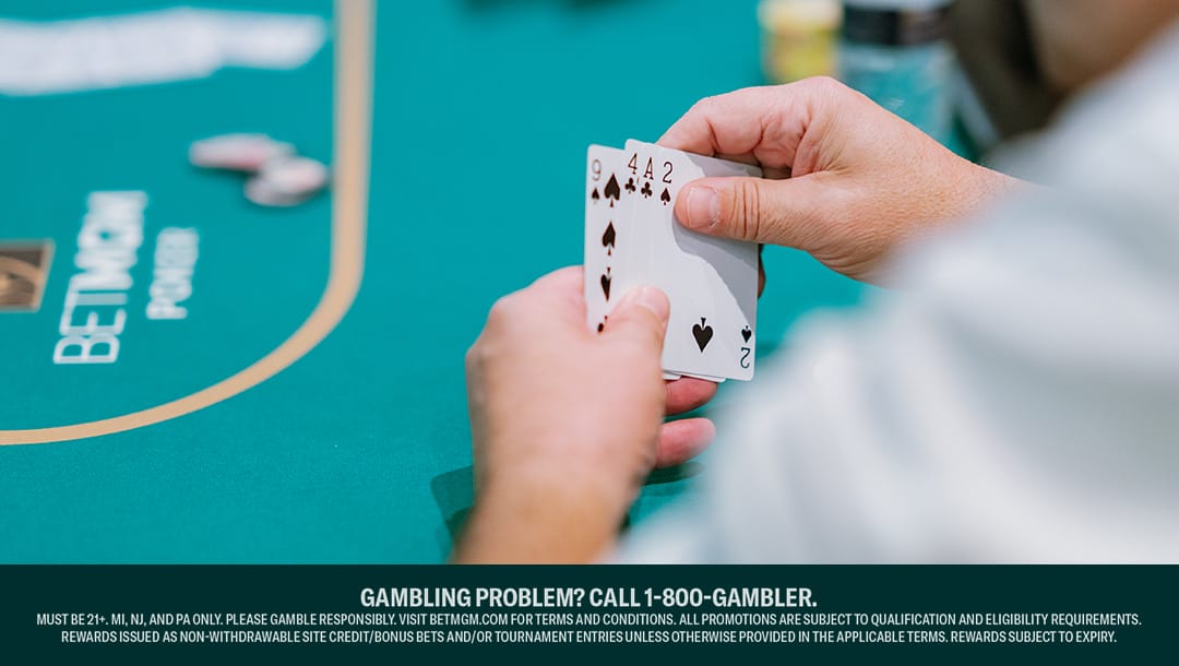 A person holds a poker hand with two aces and two fours at a poker table, with chips and card back visible.