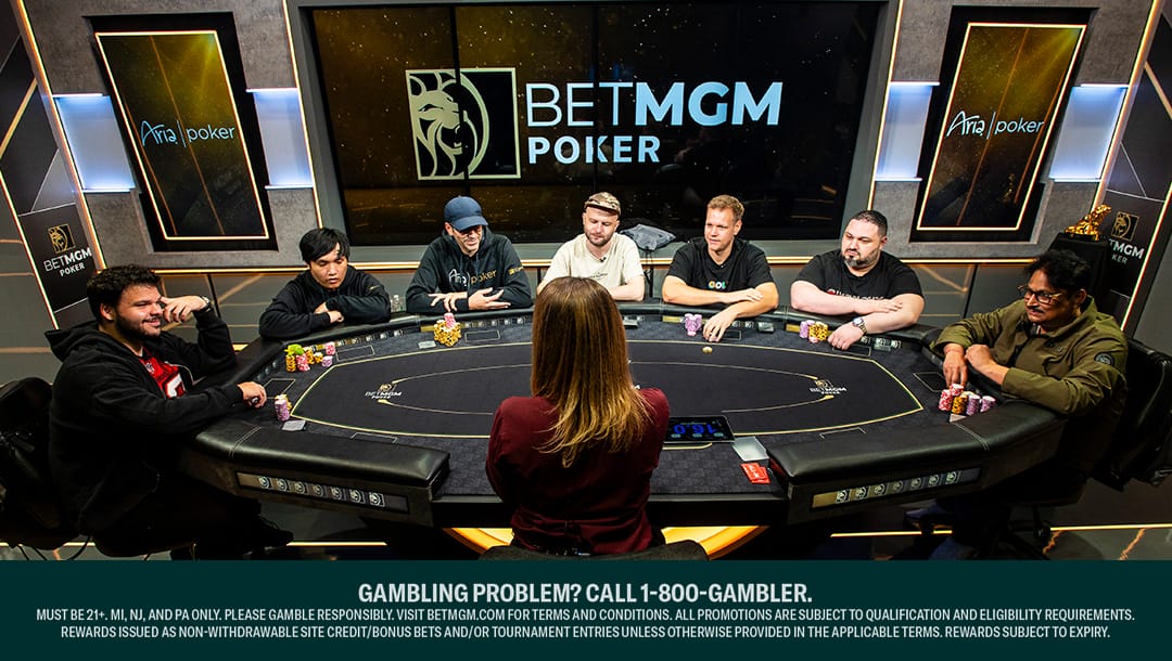 Seven poker players seated around a black felt poker table at the Aria Poker room during a BetMGM Poker event, facing a female dealer. Stacks of colorful poker chips are in front of each player, with large BetMGM Poker and Aria Poker logos displayed on the wall behind them. A responsible gambling disclaimer appears at the bottom of the image.
