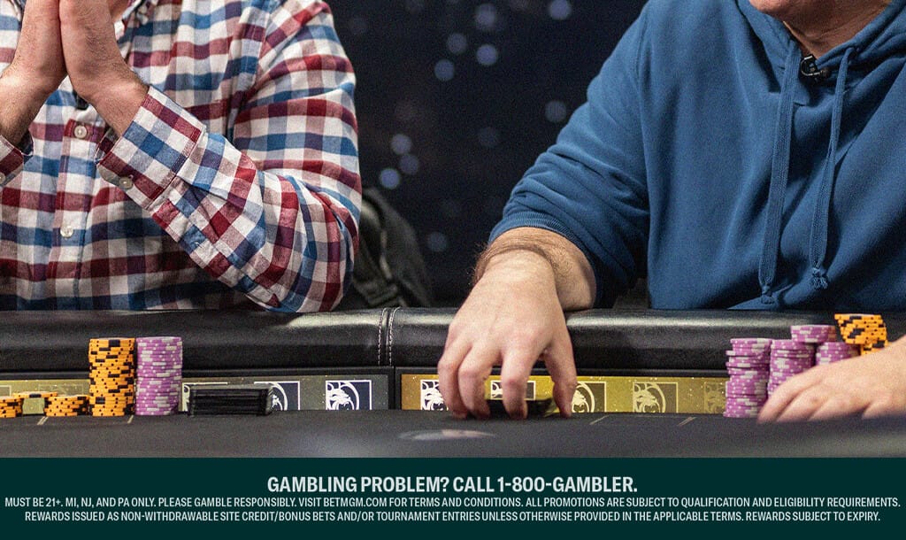 Two poker players sit at a table, focused on the game. One wears a red, white, and blue plaid shirt with hands clasped, while the other wears a blue hoodie, reaching for a stack of chips. Various colored poker chips and cards are visible on the table.