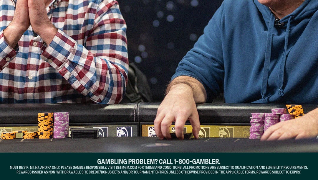 Two poker players sit at a table, focused on the game. One wears a red, white, and blue plaid shirt with hands clasped, while the other wears a blue hoodie, reaching for a stack of chips. Various colored poker chips and cards are visible on the table.